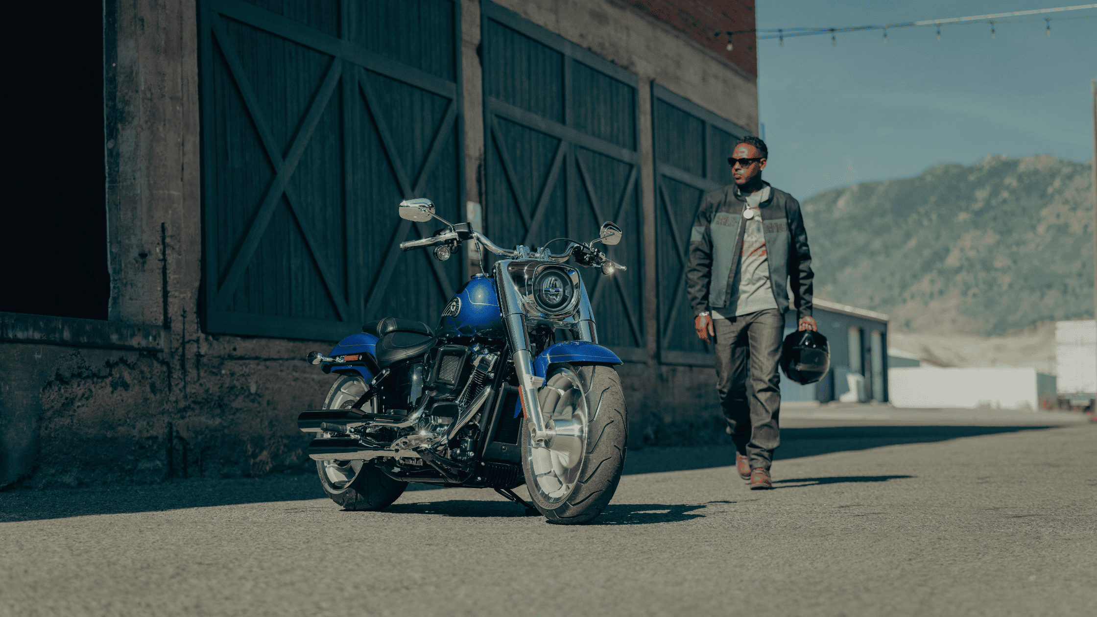 2025 Harley-Davidson® Fat Boy® blue cruiser parked outside industrial building with solid wheels