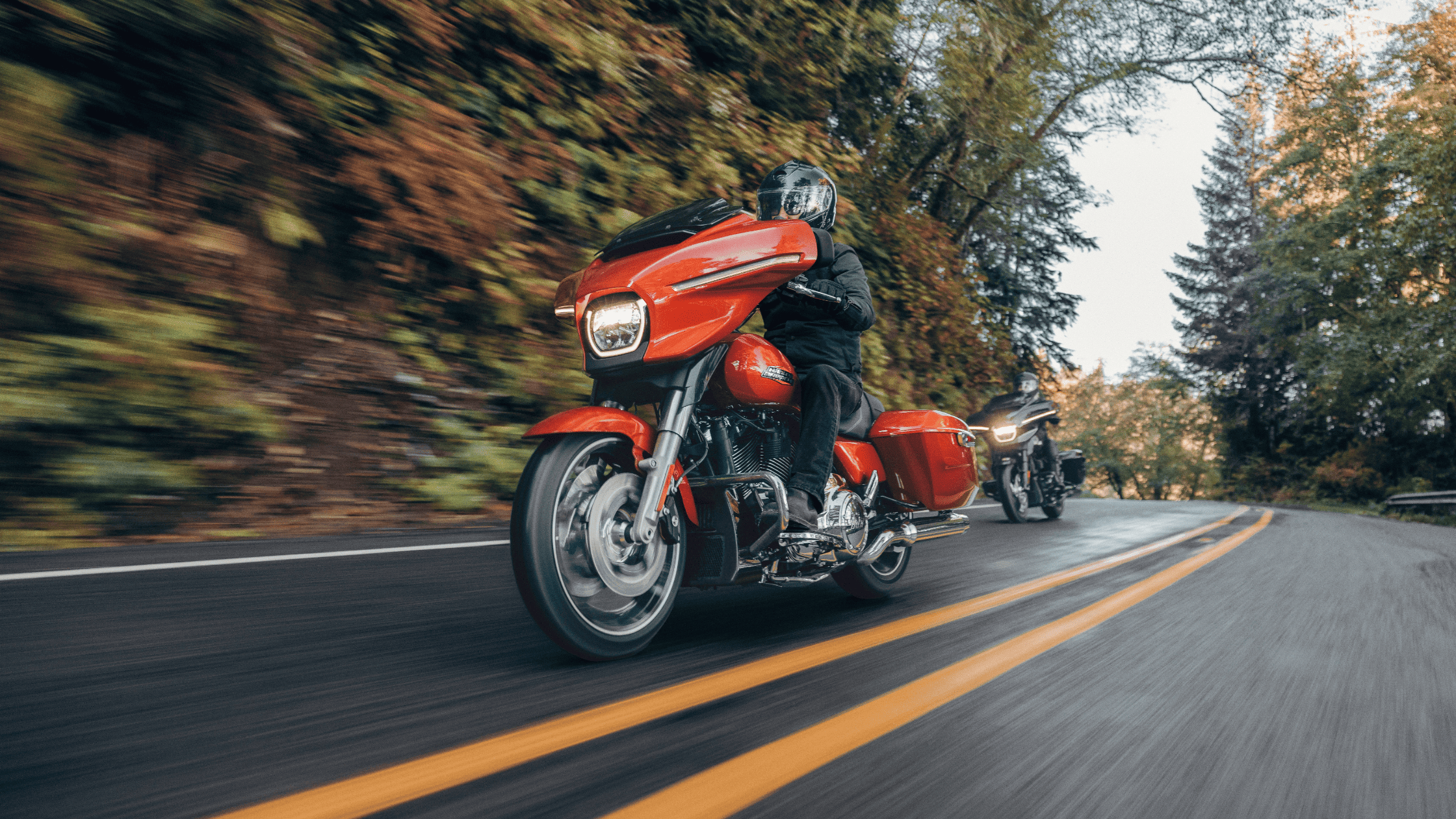 2025 Harley-Davidson Street Glide in bright red color riding on forested twisty mountain road