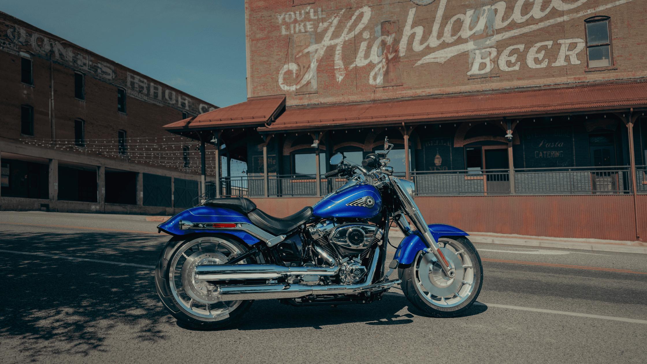 2025 Harley-Davidson® Fat Boy® parked on street in front of Highlander Beer mural building