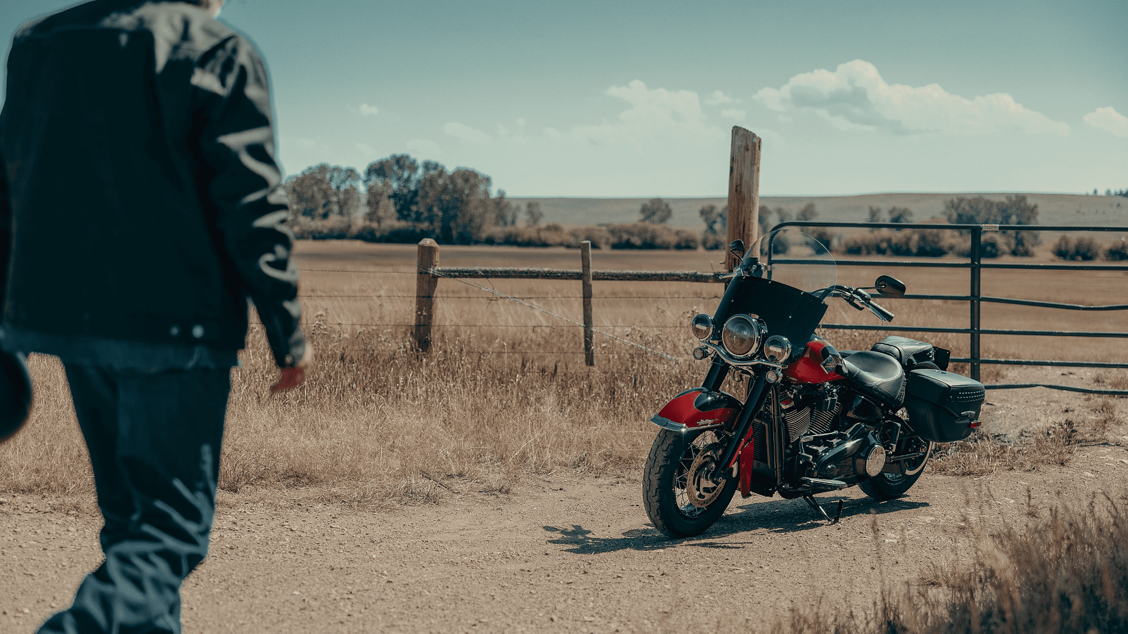 2025 Harley-Davidson® Heritage Classic near fence in rural field as rider approaches on foot.
