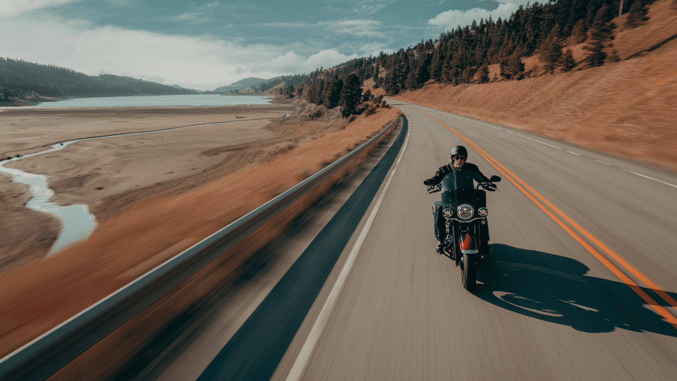2025 Harley-Davidson® Heritage Classic riding scenic highway beside lake and forest landscape