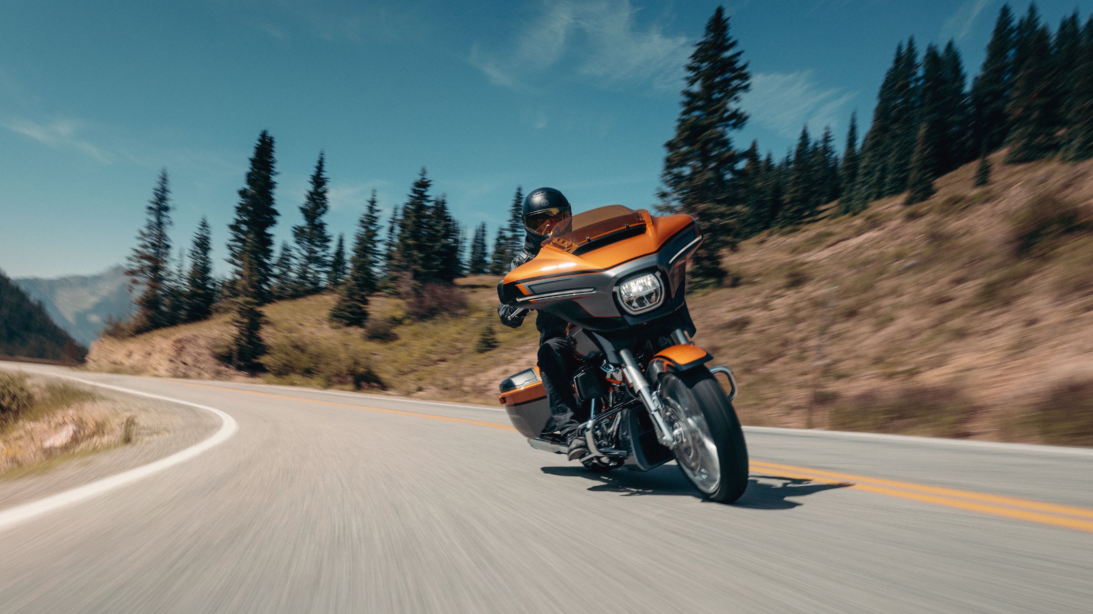 Orange 2026 Harley-Davidson® CVO™ Street Glide® leaning through mountain curve with solo rider