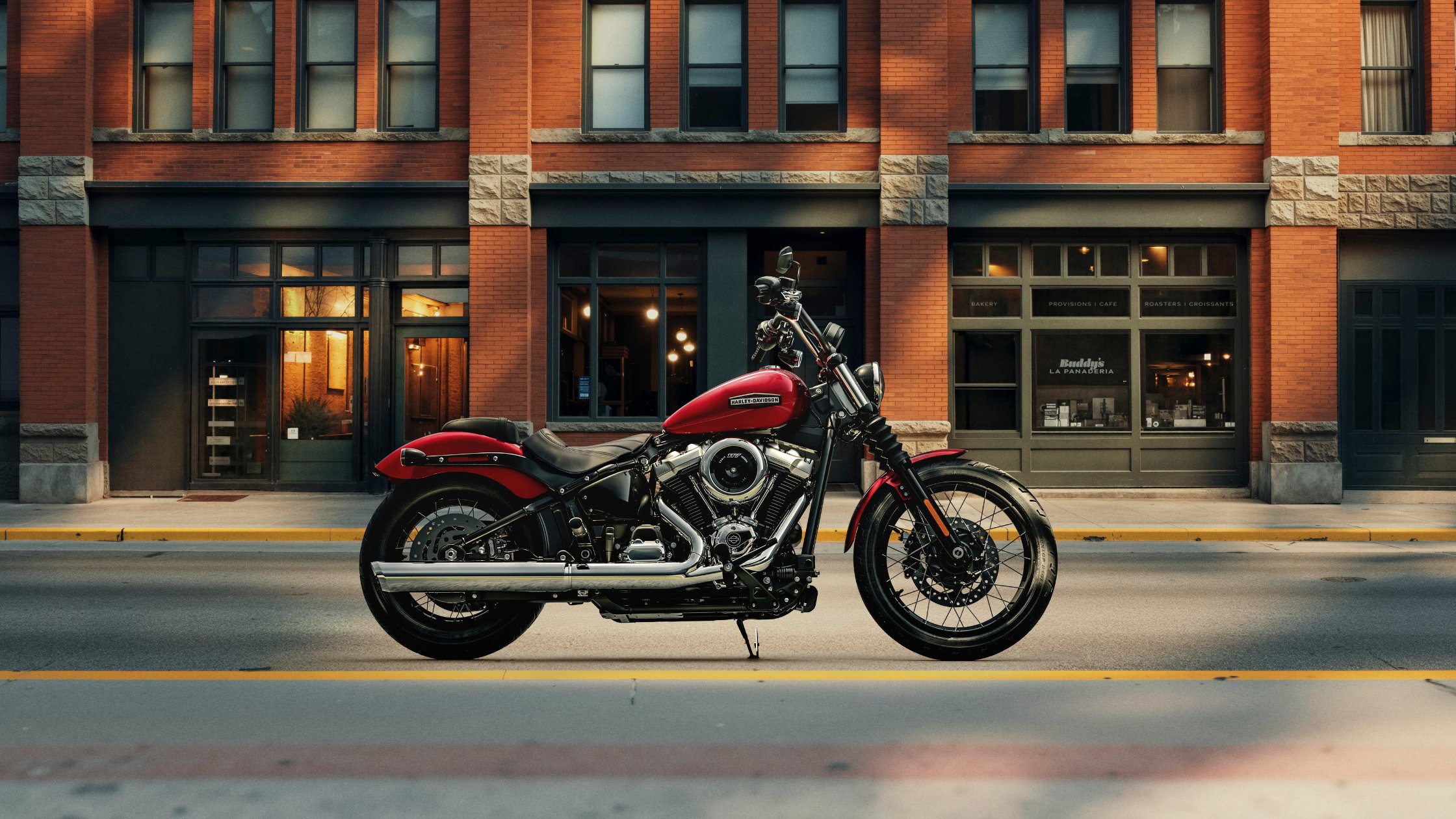 Red 2026 Harley-Davidson® Street Bob® parked on a city street in front of brick storefronts
